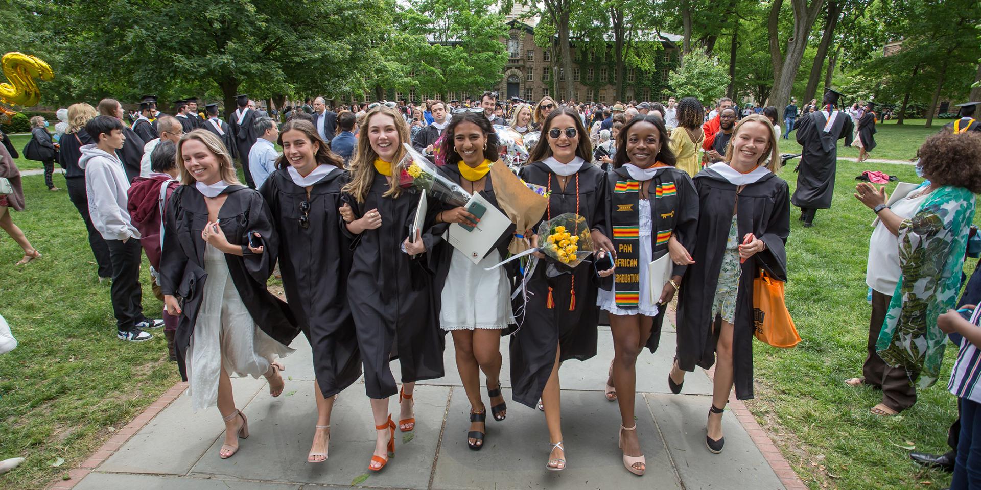 Newly-graduated alumna link arms and walk towards FitzRandolph Gate